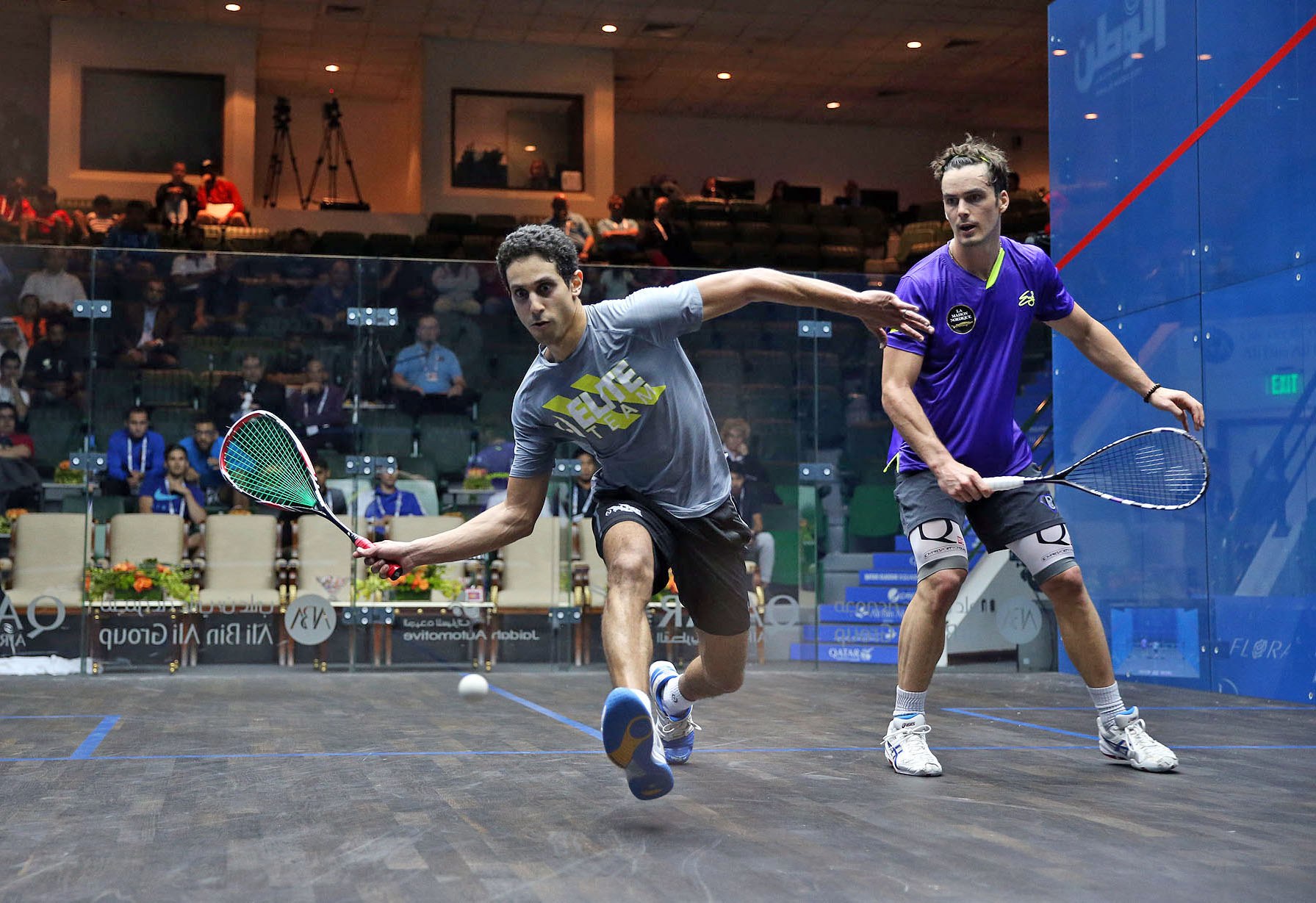 Players rallying inside a glass-walled squash court during a competitive match